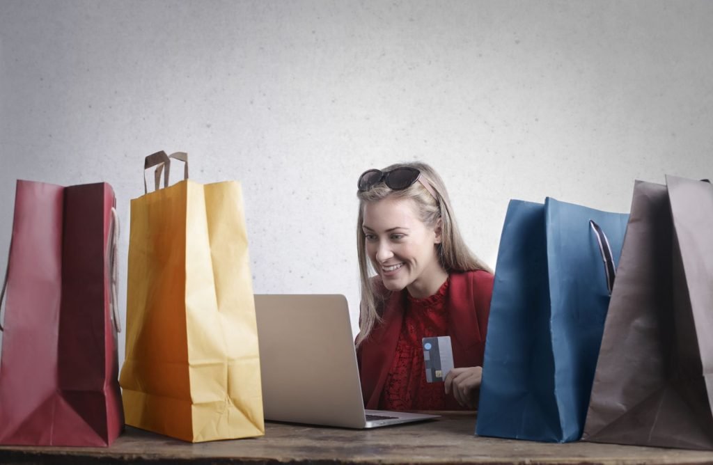Mujer comprando en línea rodeada de bolsas de compras