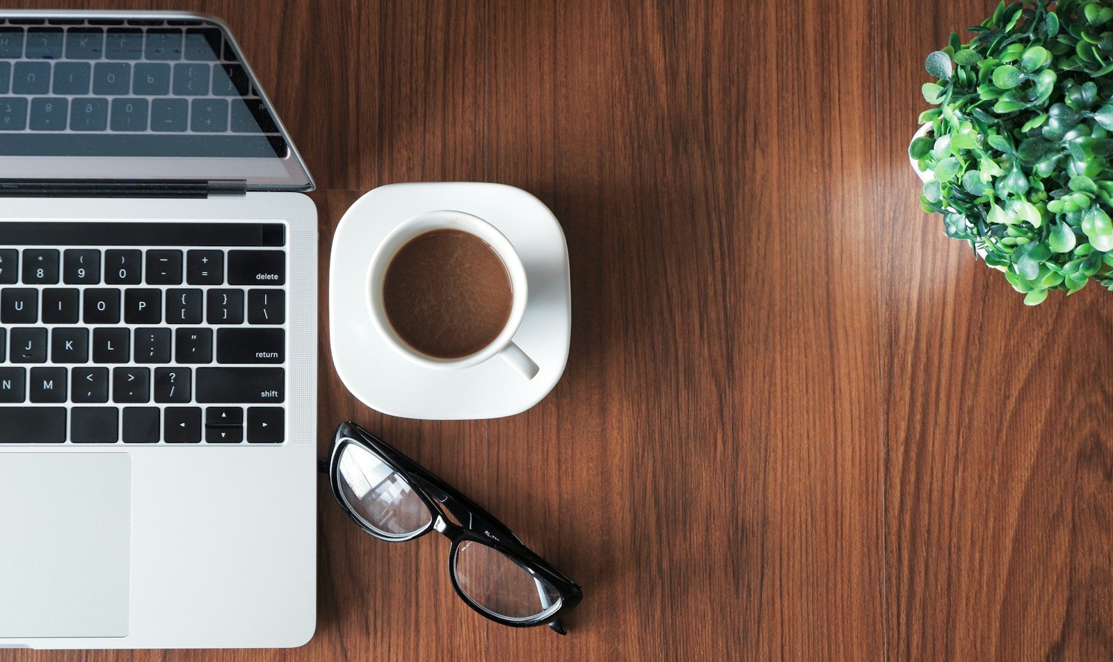 Laptop, taza de café y lentes sobre un escritorio de madera